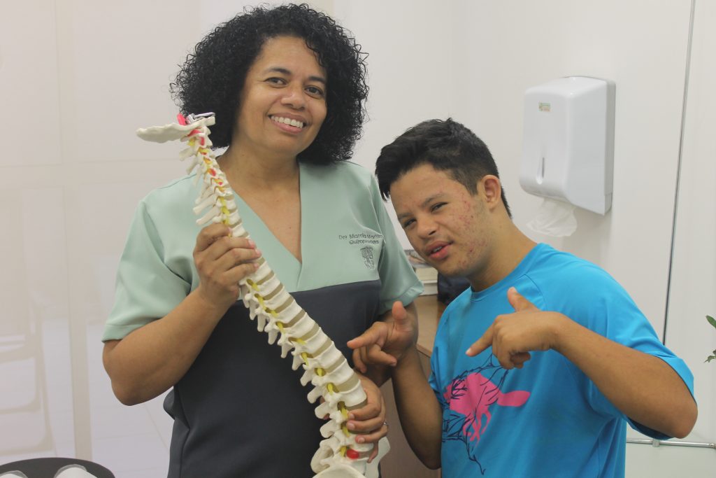 Dra Marcia Martim, quiropraxista, com seu paciente, Samuel. Dra Marcia está segurando um modelo de coluna vertebral.